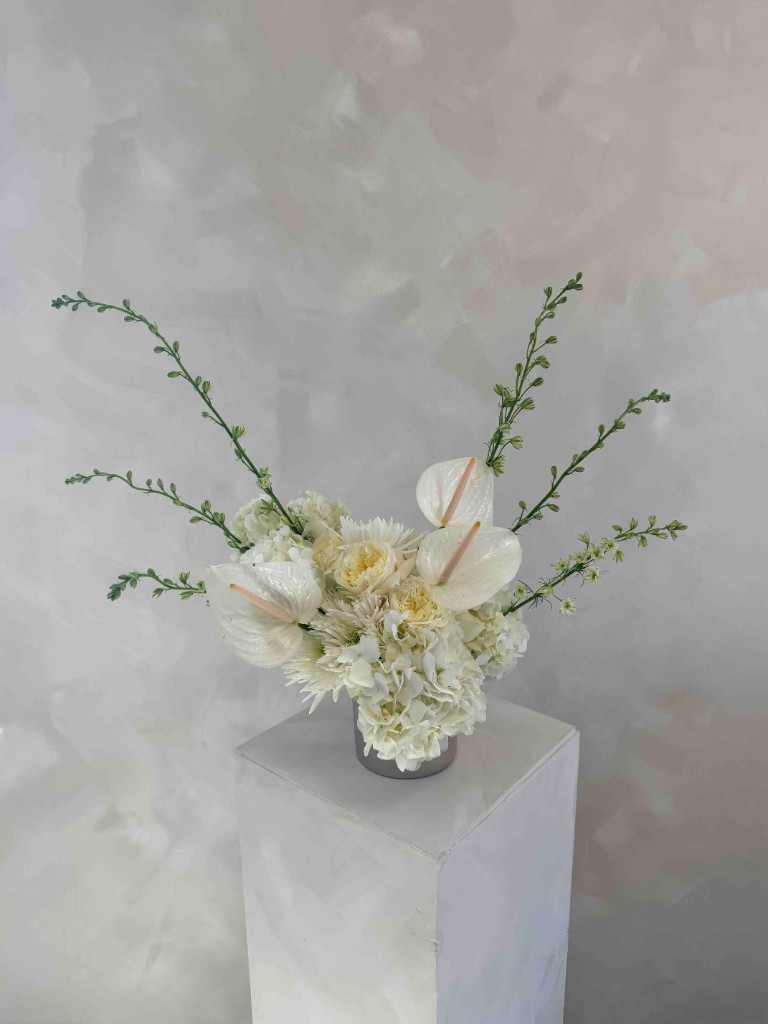 White floral arrangement with anthuriums, hydrangeas and roses in a metallic vase on pedestal