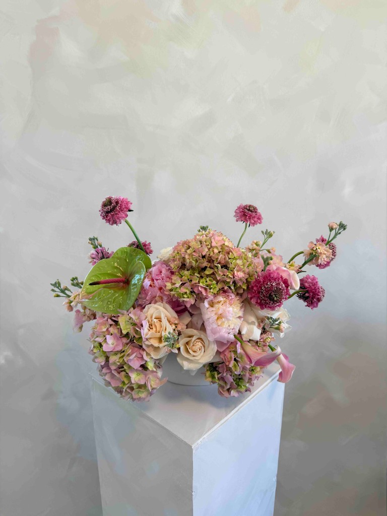 Arrangement of pink and cream hydrangeas, roses and green anthurium in a white bowl on pedestal