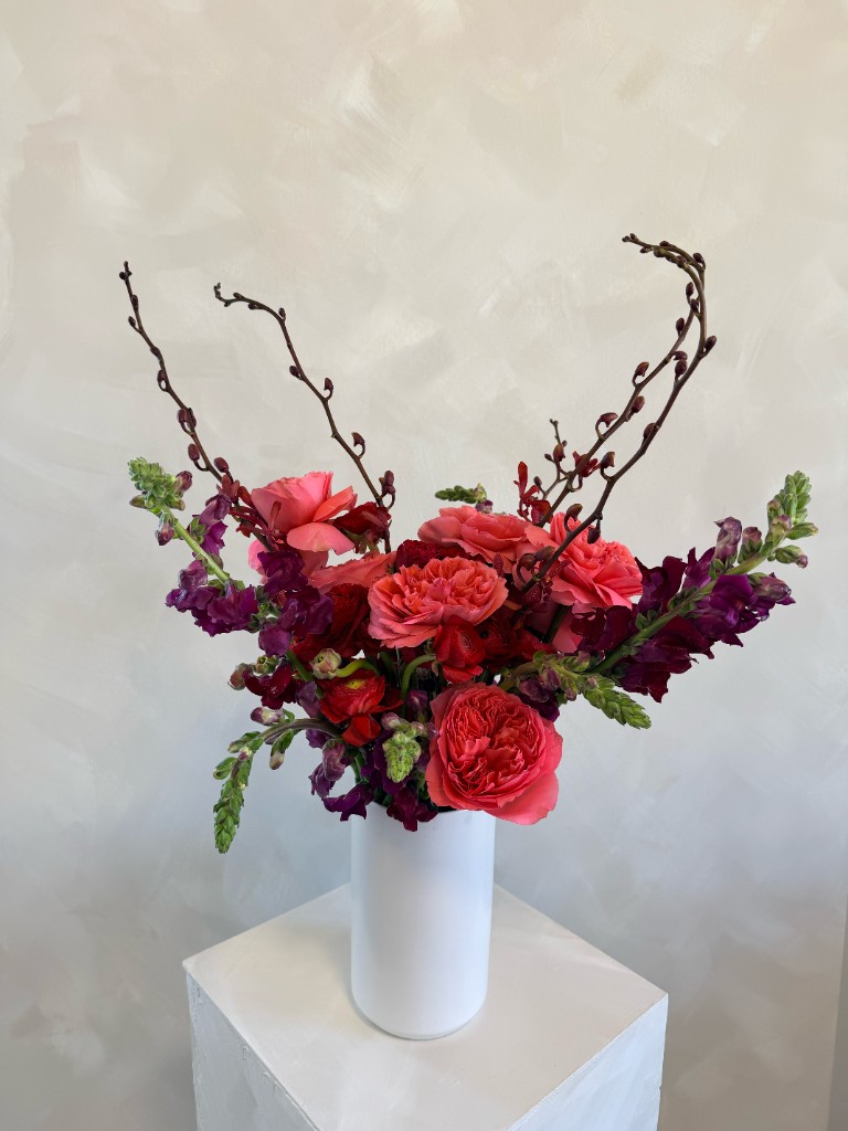 Floral arrangement with roses, snapdragons and branches in a white vase