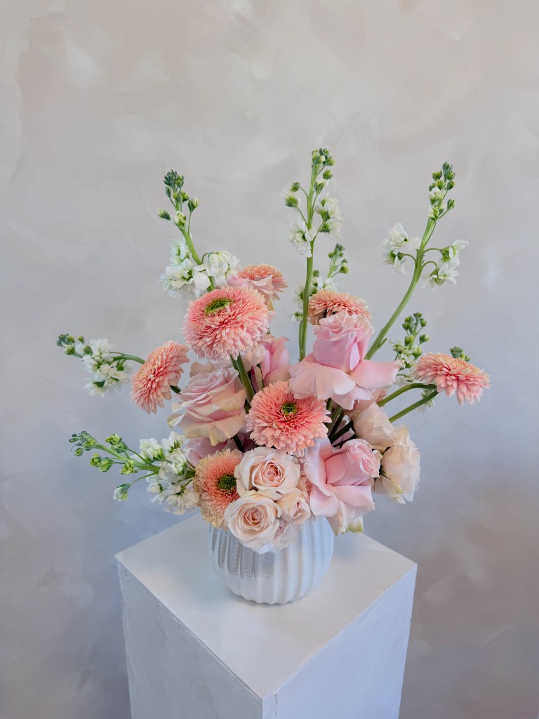 Bouquet of pink and peach blooms with white flowers in a ribbed white vase