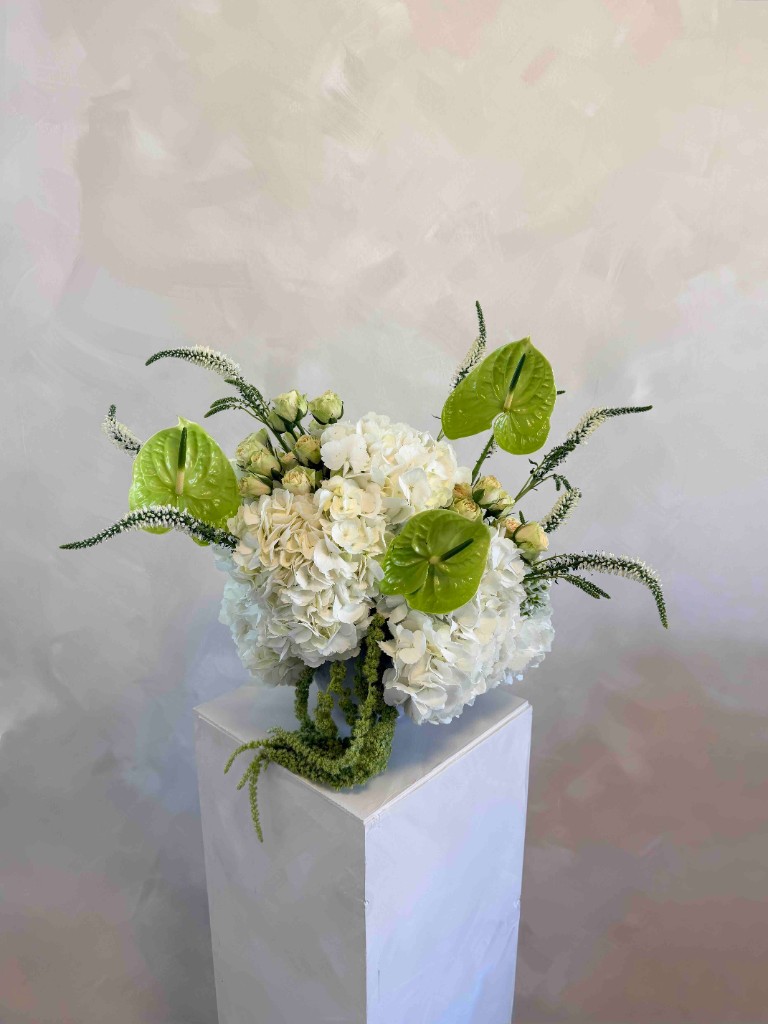 White hydrangea arrangement with green anthuriums and trailing greenery on a pedestal